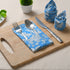 Blue floral napkin placed under silverware on wooden serving tray, with matching napkins rolled beside.
