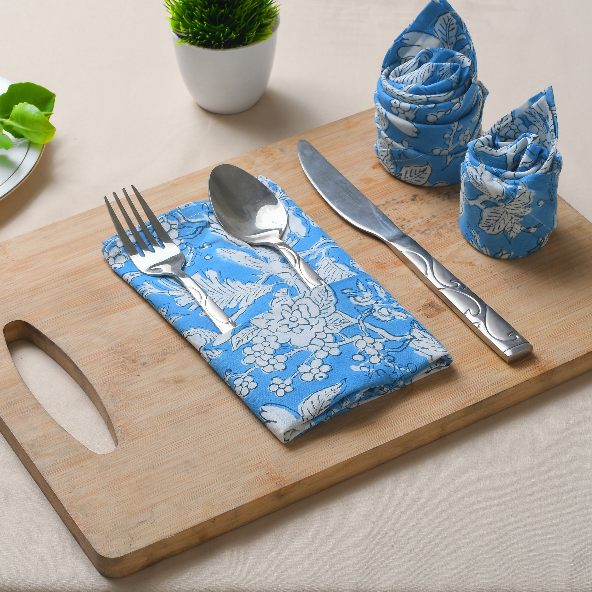 Blue floral napkin placed under silverware on wooden serving tray, with matching napkins rolled beside.