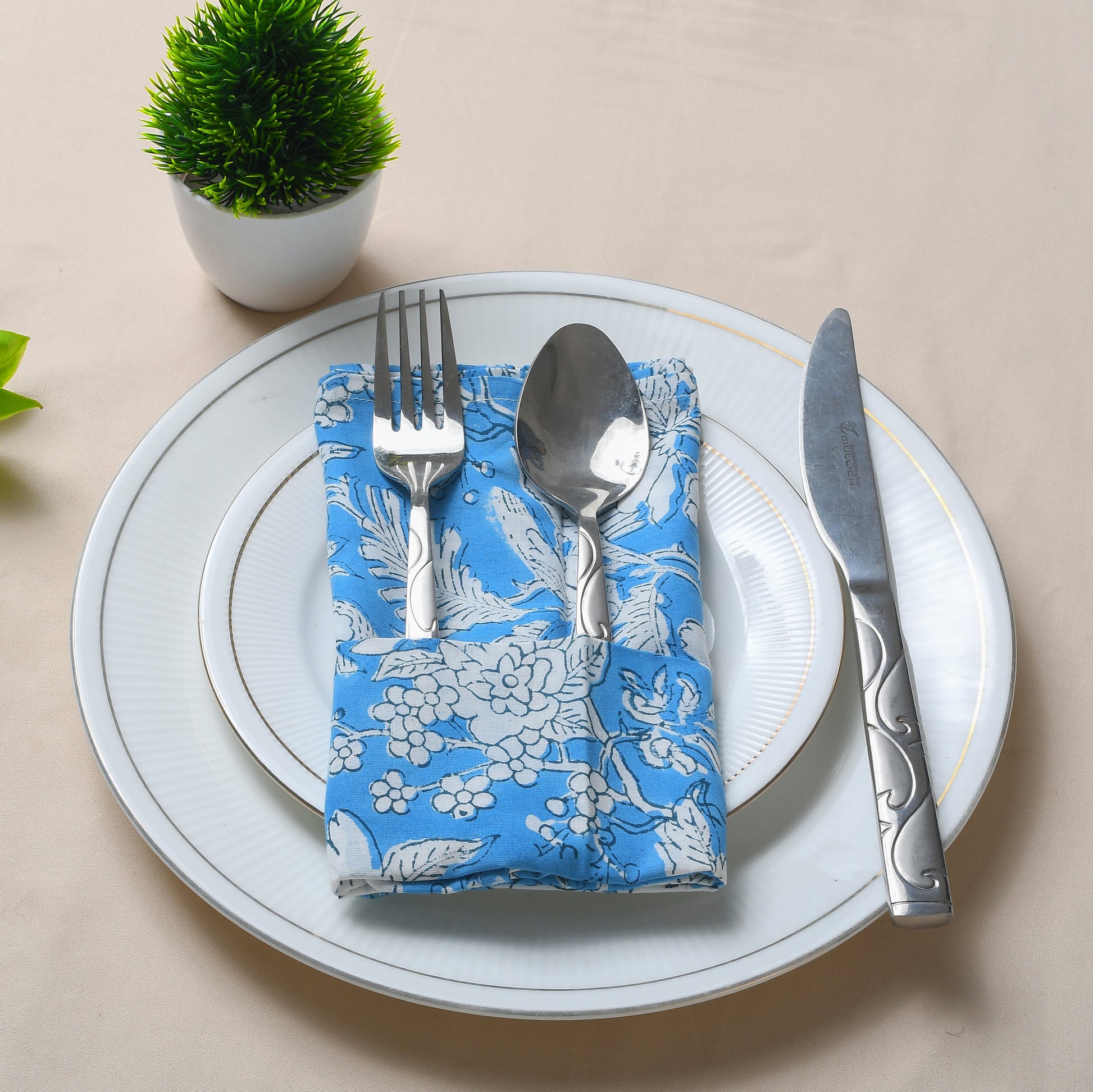 Single blue floral napkin folded under silverware on a white plate.