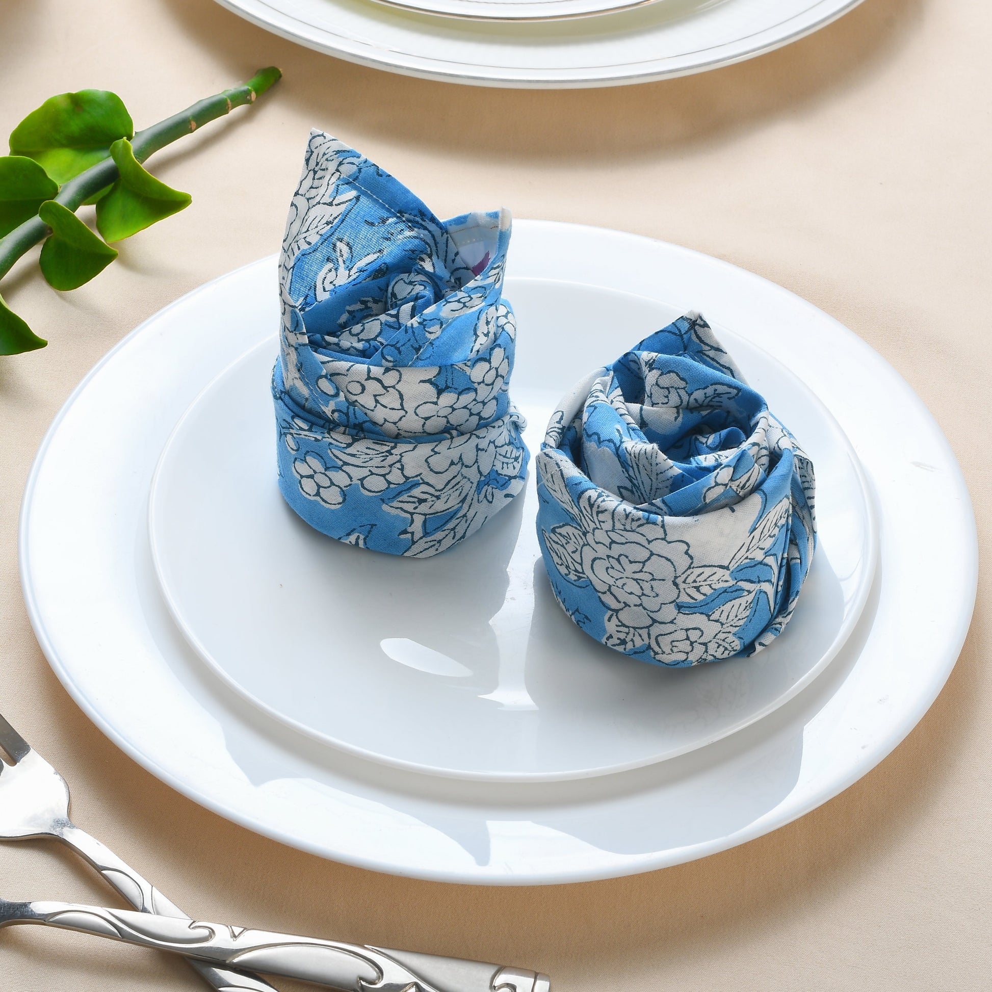 Two rolled floral napkins styled vertically on a white plate.