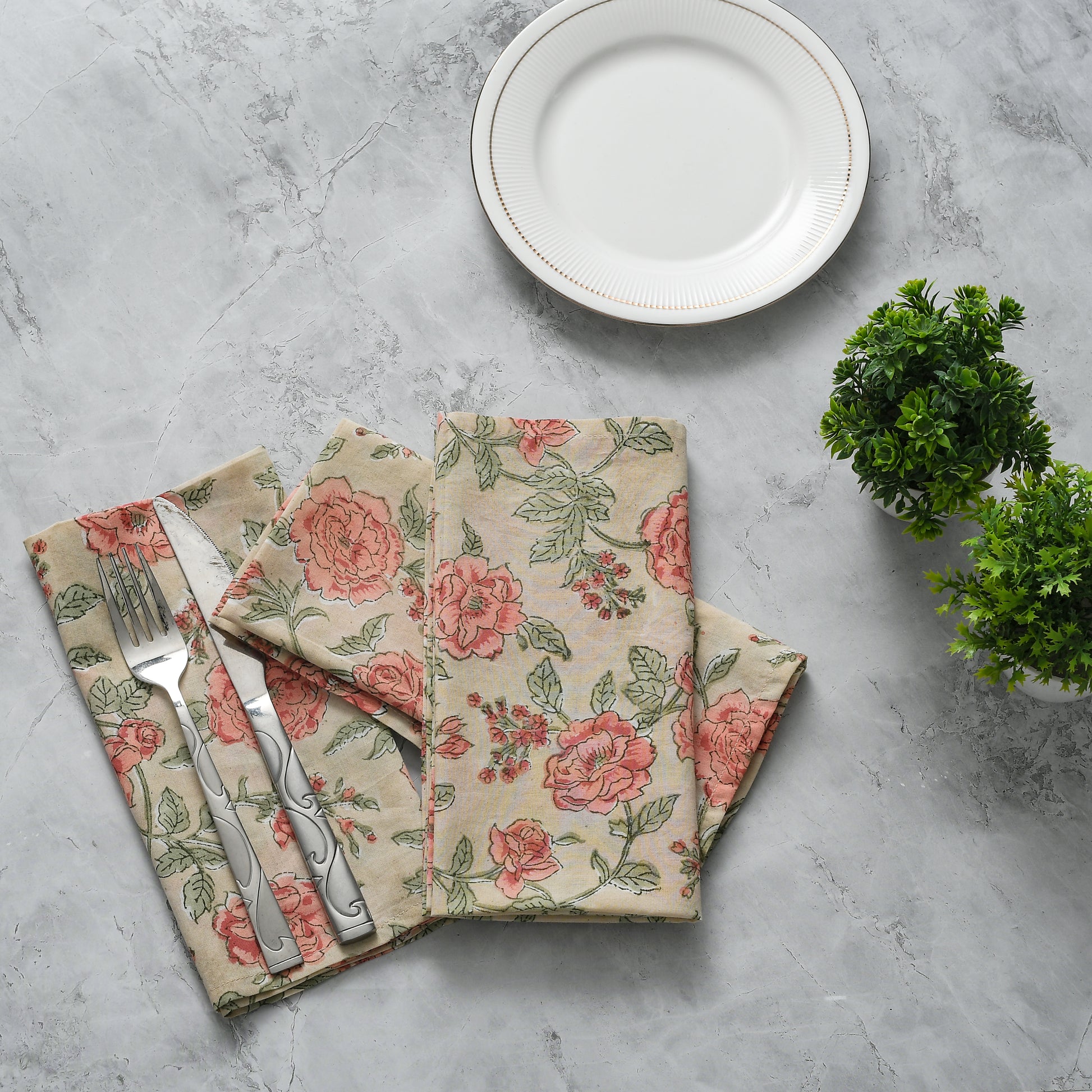 Elegant place setting with two tan and pink floral napkins and silverware arranged creatively.