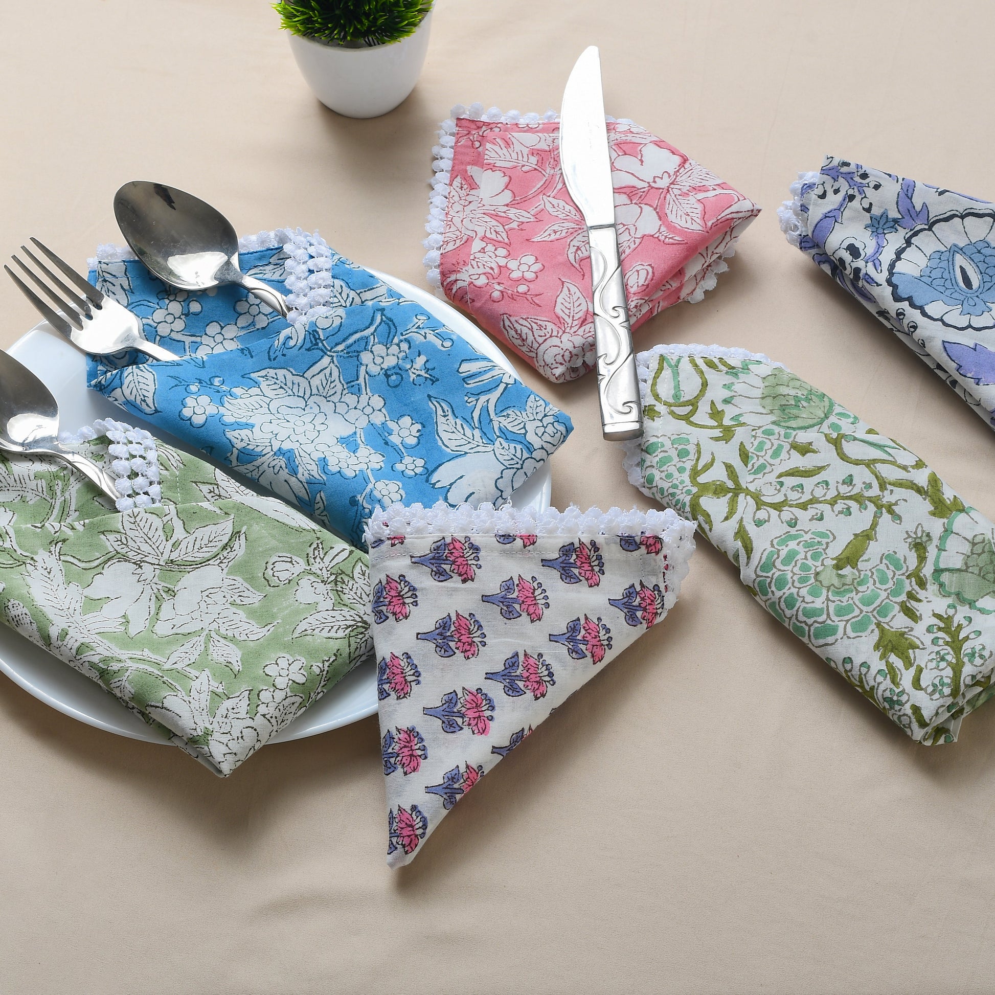 Four cotton napkins in assorted floral prints folded with silverware on a white plate.