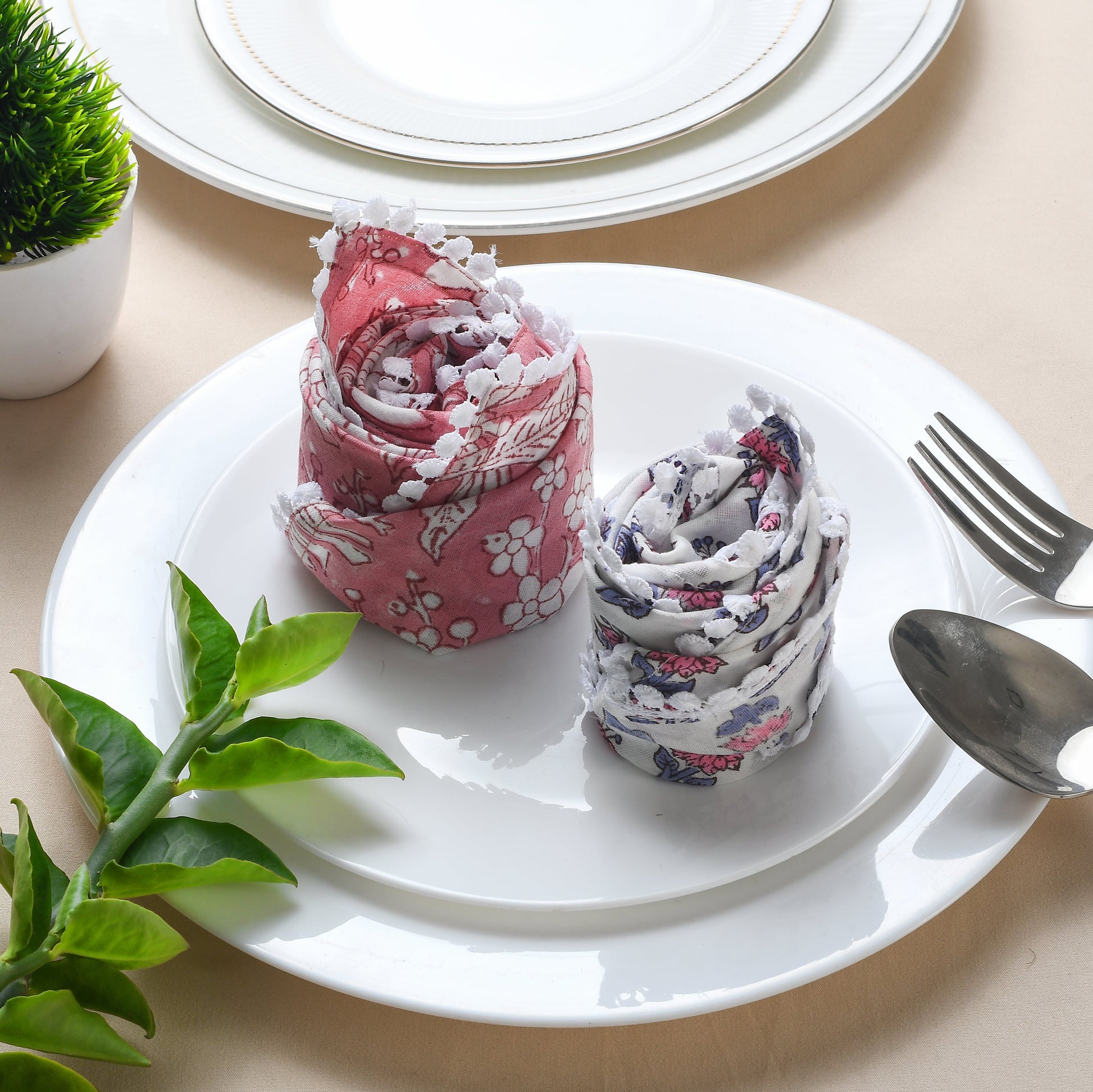 2 Rolled floral napkin placed upright on a white plate with silverware.