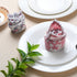 Rolled multicolor napkin on white plate with green foliage and fork.