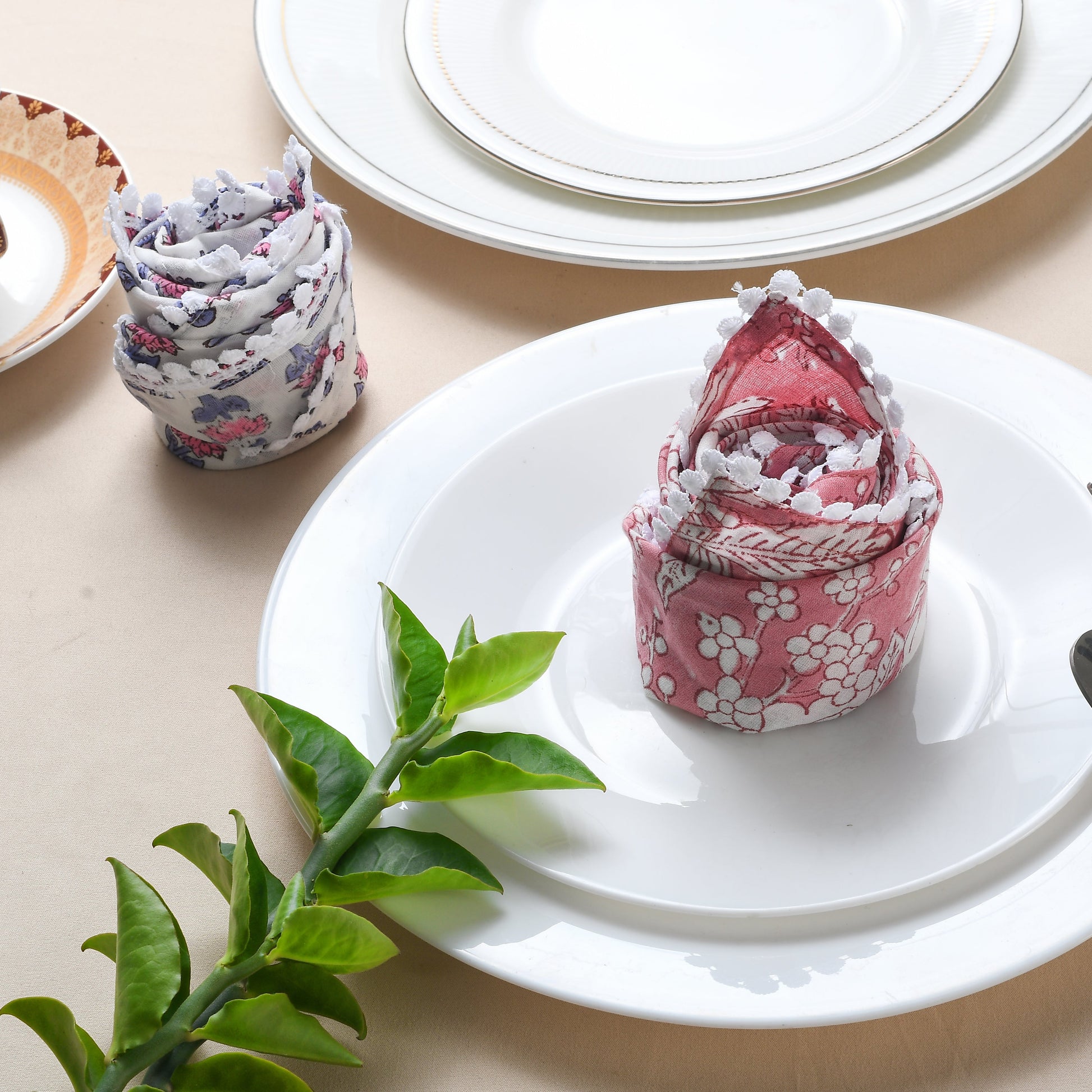 Rolled multicolor napkin on white plate with green foliage and fork.