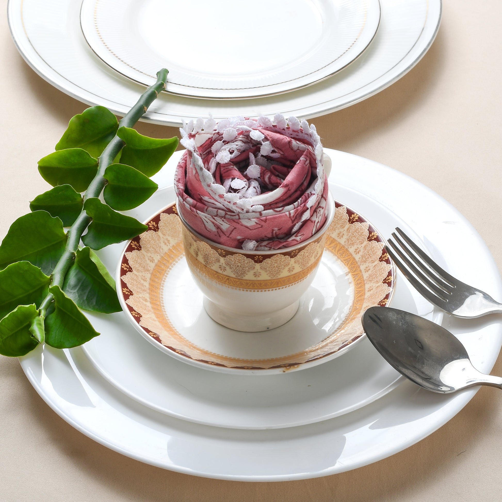 Rolled multicolor napkin on white plate with green foliage and fork.
