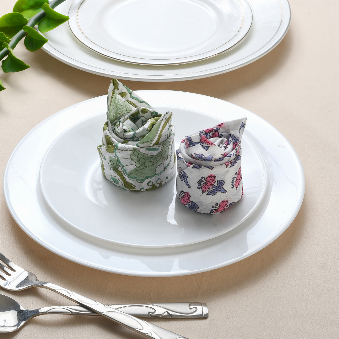 Rolled multicolor napkin on white plate with green foliage and fork.