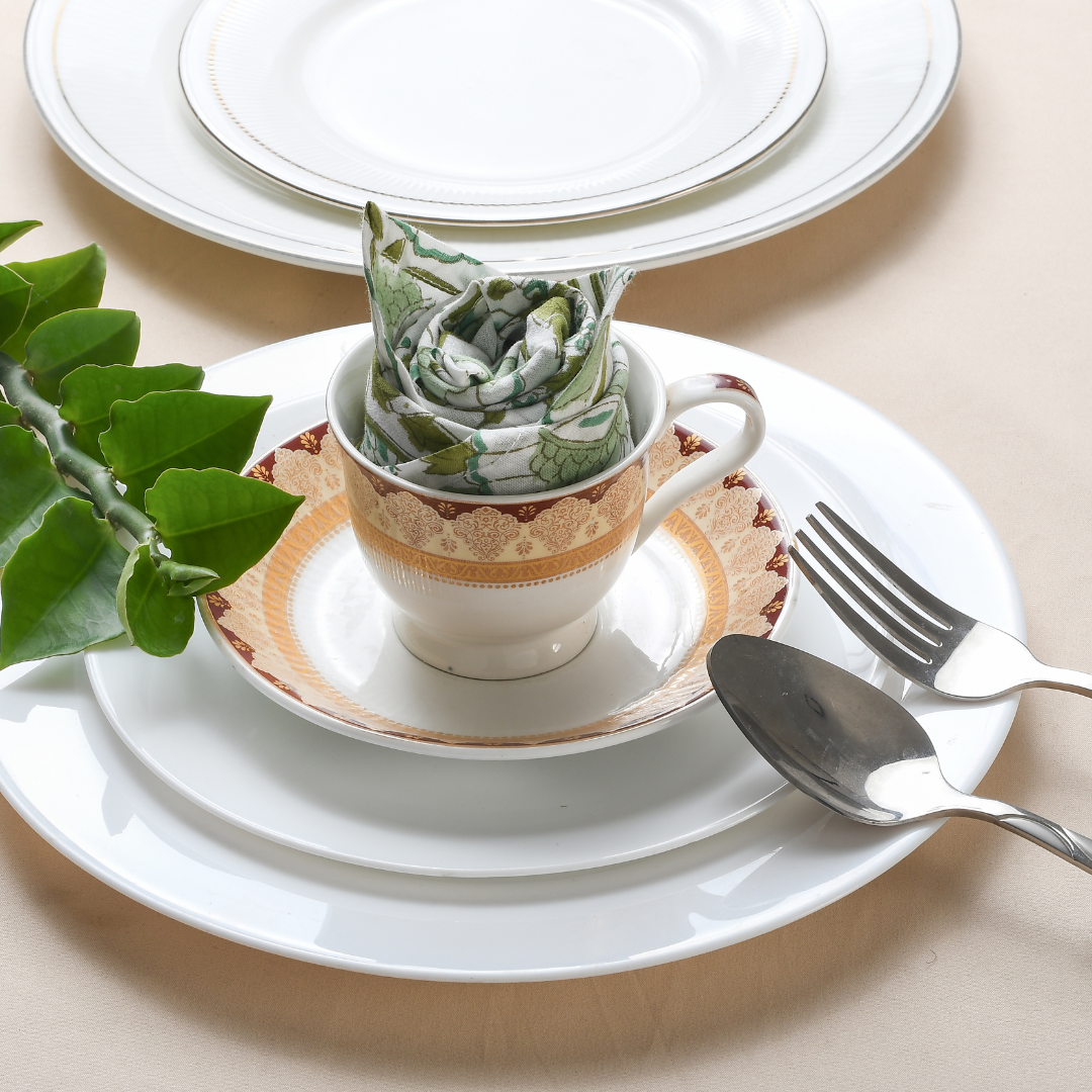 Rolled multicolor napkin on white plate with green foliage and fork.