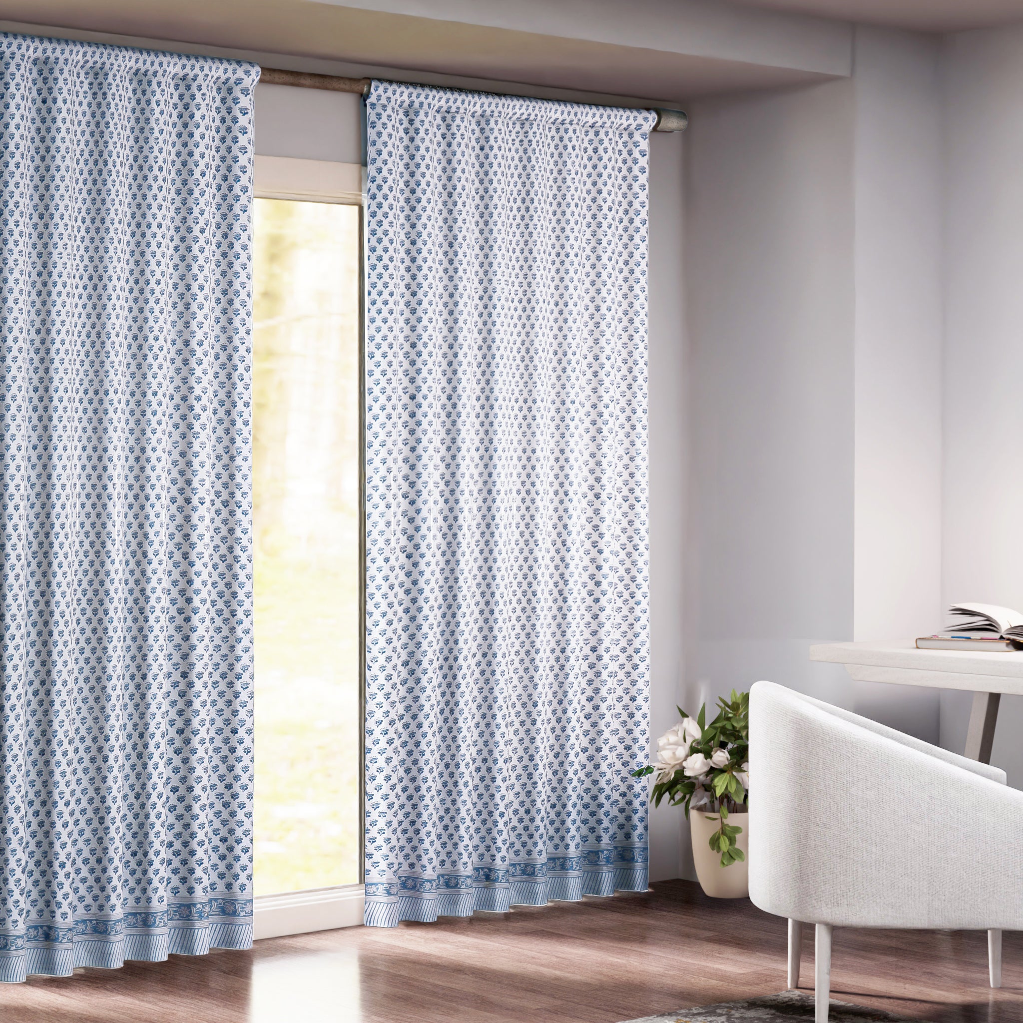 A pair of semi-sheer blue cotton block print curtains hanging in a room with a light coming through, showcasing a boho-chic design.