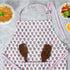 pink and white kitchen apron laying on the counter with wooden kitchen utensils in the front pocket