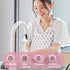 lady washing dishes and wearing a pink and white floral block print apron thats breathable, has wide coverage, washable, and stylish and comfortable