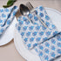 Single blue floral napkin folded under silverware on a white plate.