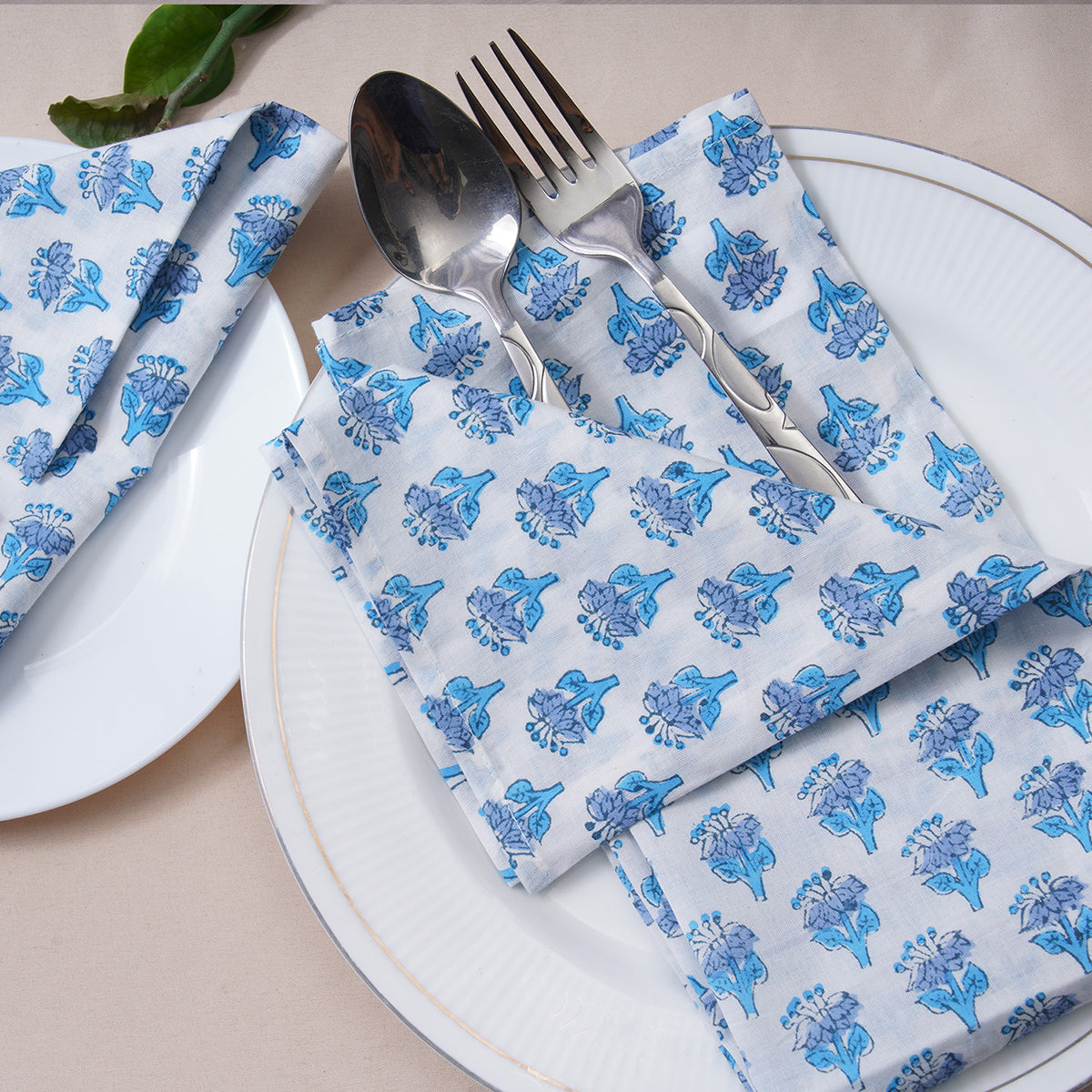 Single blue floral napkin folded under silverware on a white plate.