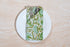 Single green floral napkin wrapped around silverware on a white plate.