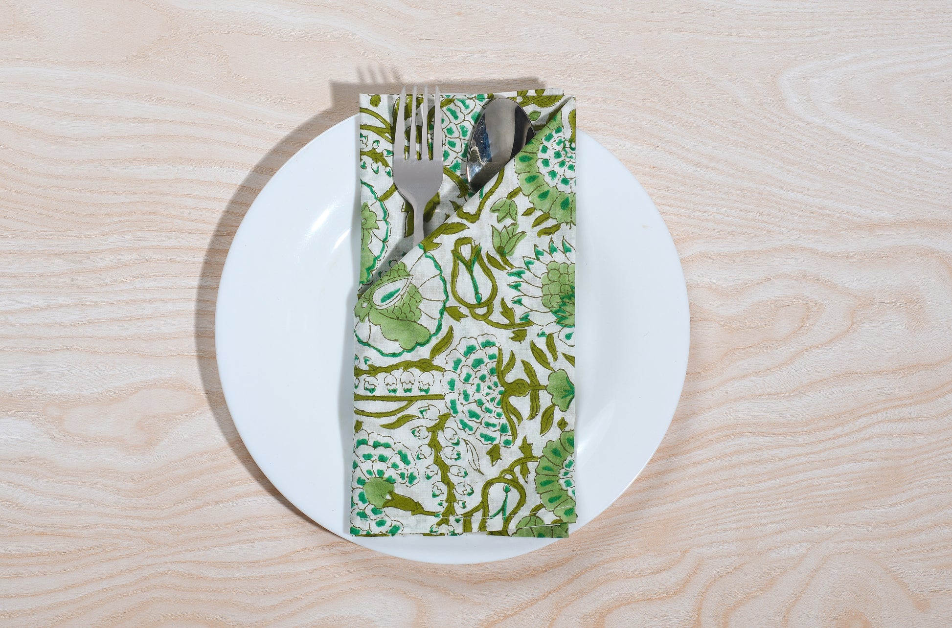 Single green floral napkin wrapped around silverware on a white plate.