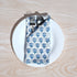 Single blue floral napkin wrapped around silverware on a white plate.