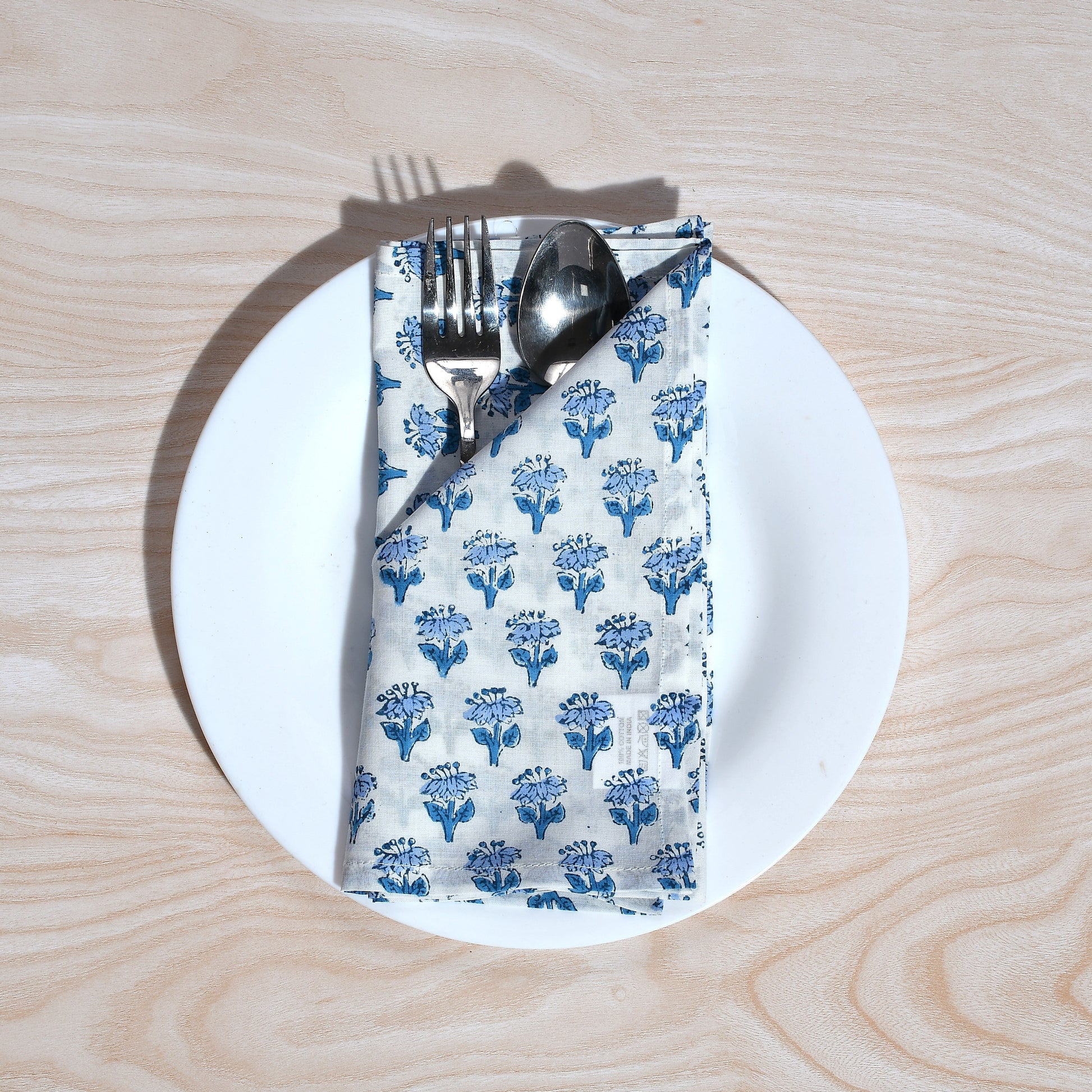 Single blue floral napkin wrapped around silverware on a white plate.
