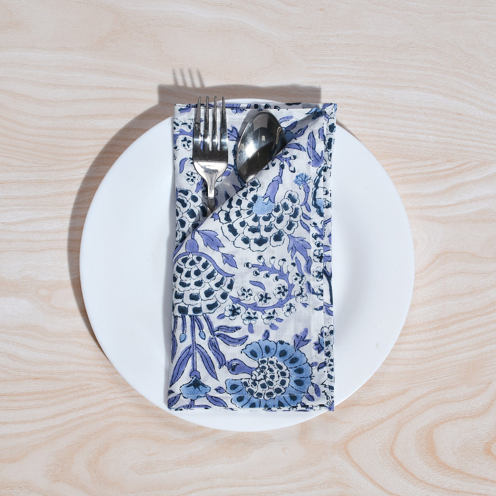 Single blue floral napkin wrapped around silverware on a white plate.