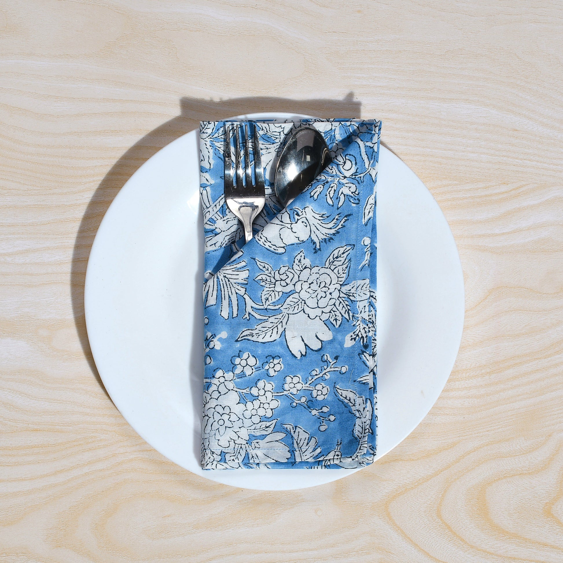 Single blue floral napkin wrapped around silverware on a white plate.