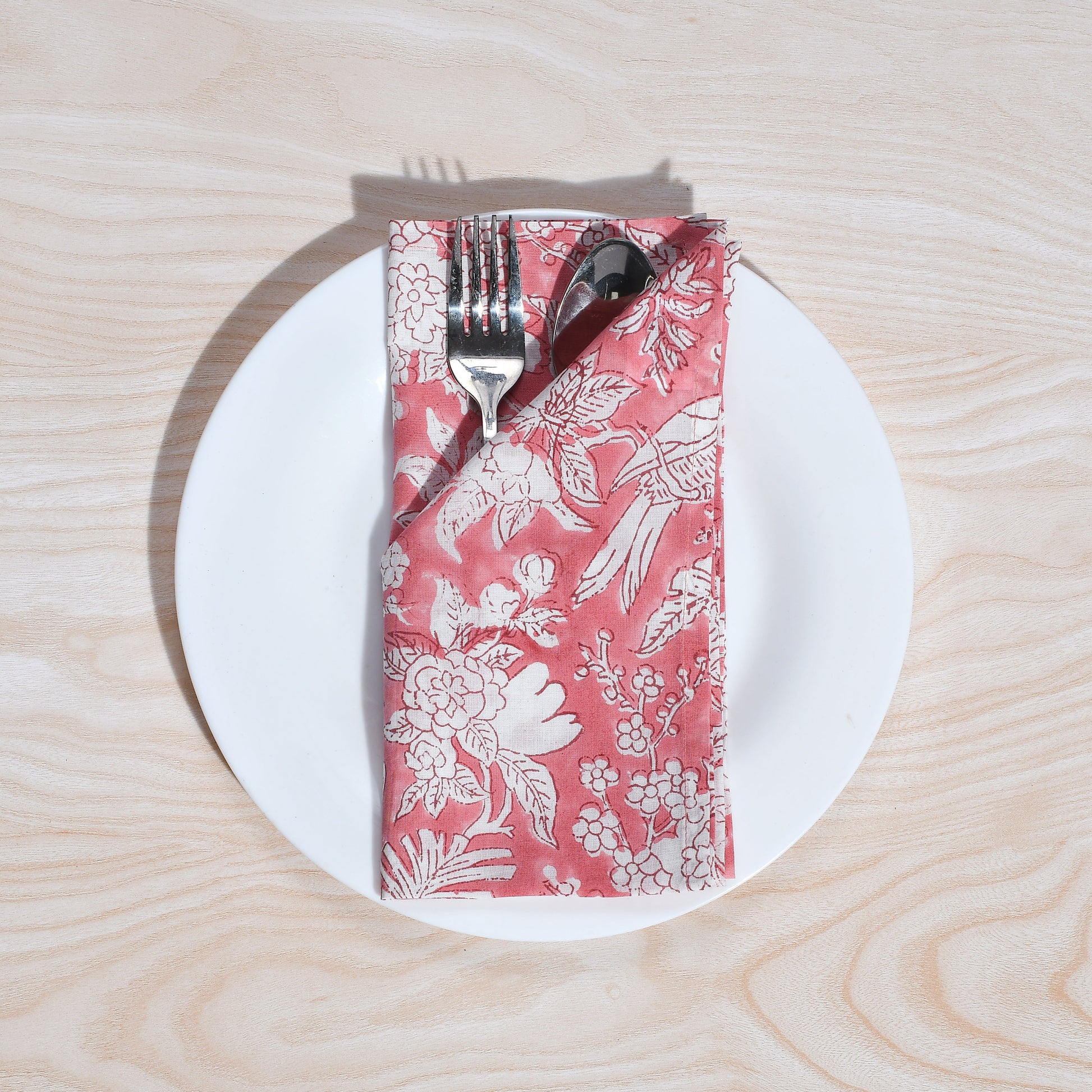 Single pink floral napkin wrapped around silverware on a white plate.