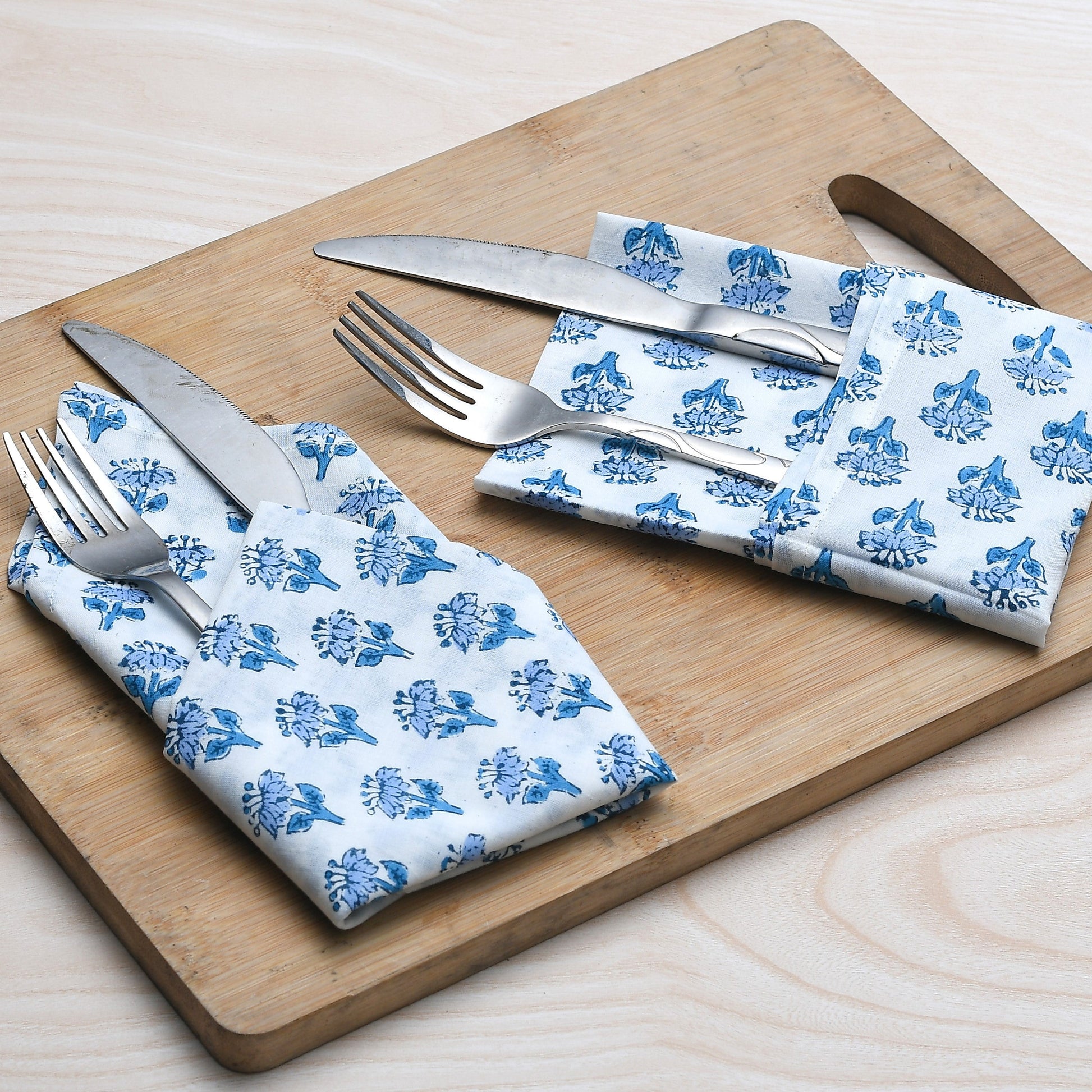 Blue floral napkin placed under silverware on wooden serving tray, with matching napkins rolled beside.