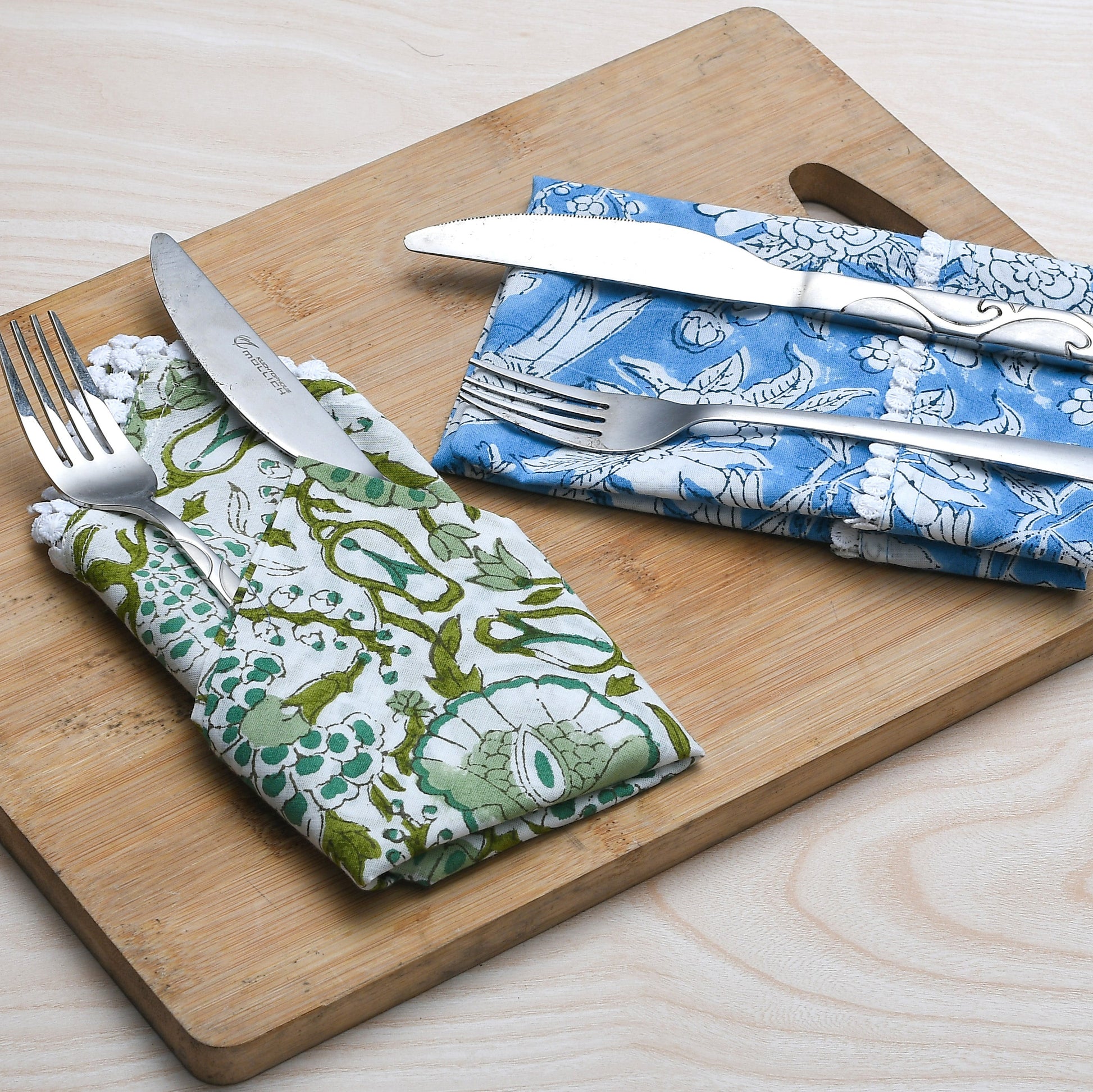 Blue and green floral napkins folded with silverware on a wooden serving tray.