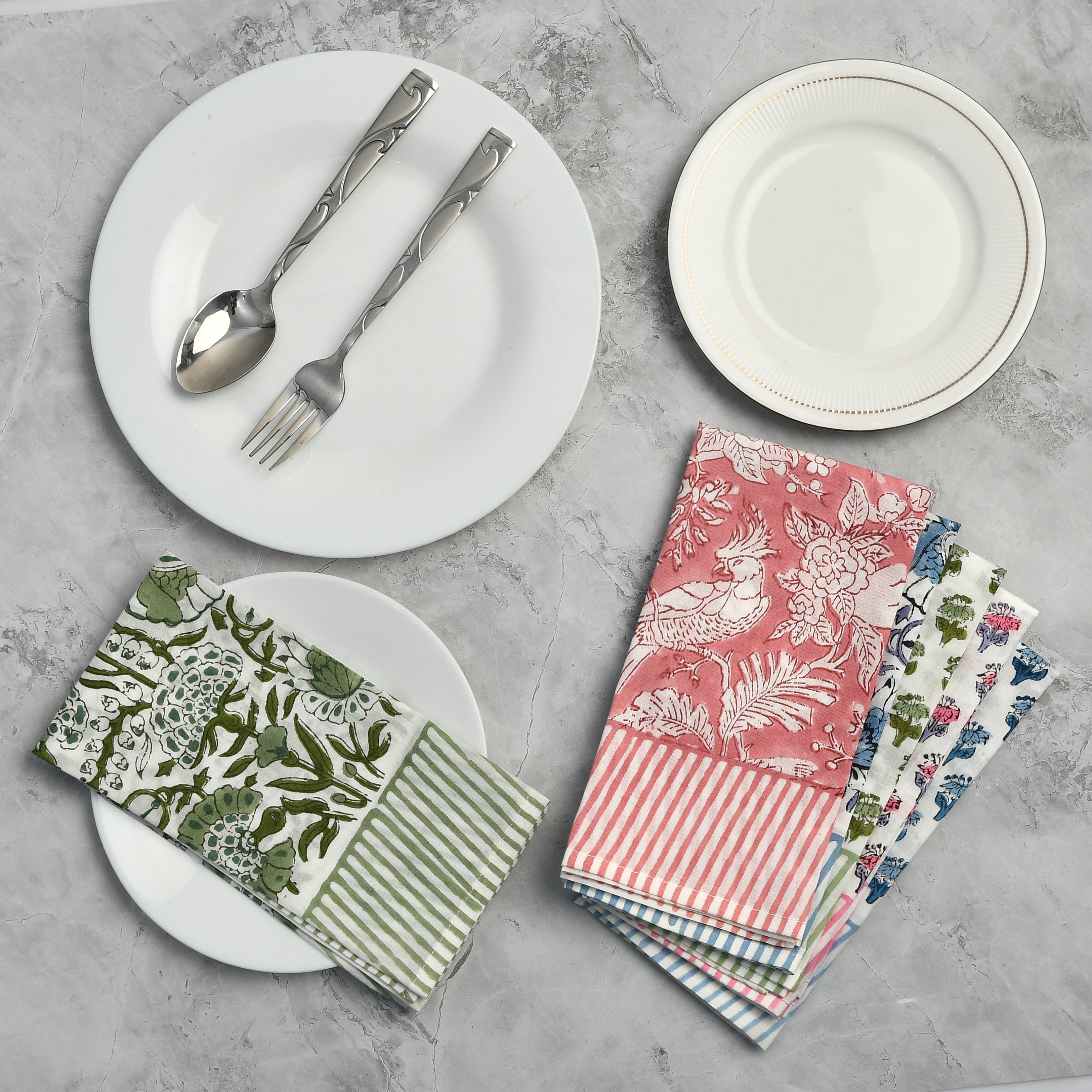 A collection of colorful cotton cloth napkins with striped border, displayed on a table alongside white plates and cutlery.