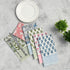 Four cotton napkins in assorted floral prints folded with silverware on a white plate.