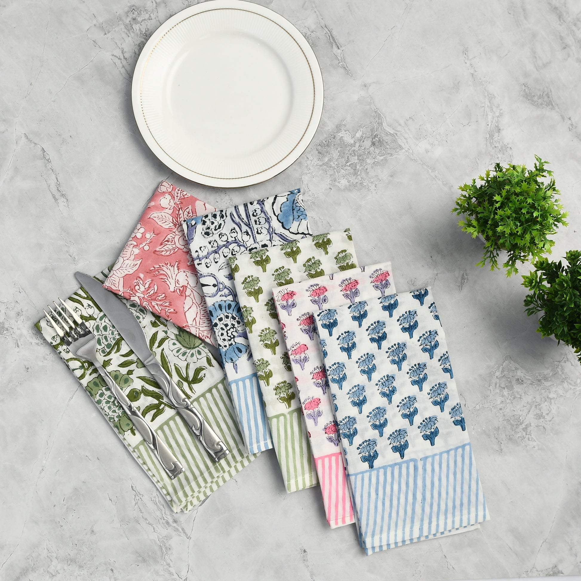 Four cotton napkins in assorted floral prints folded with silverware on a white plate.