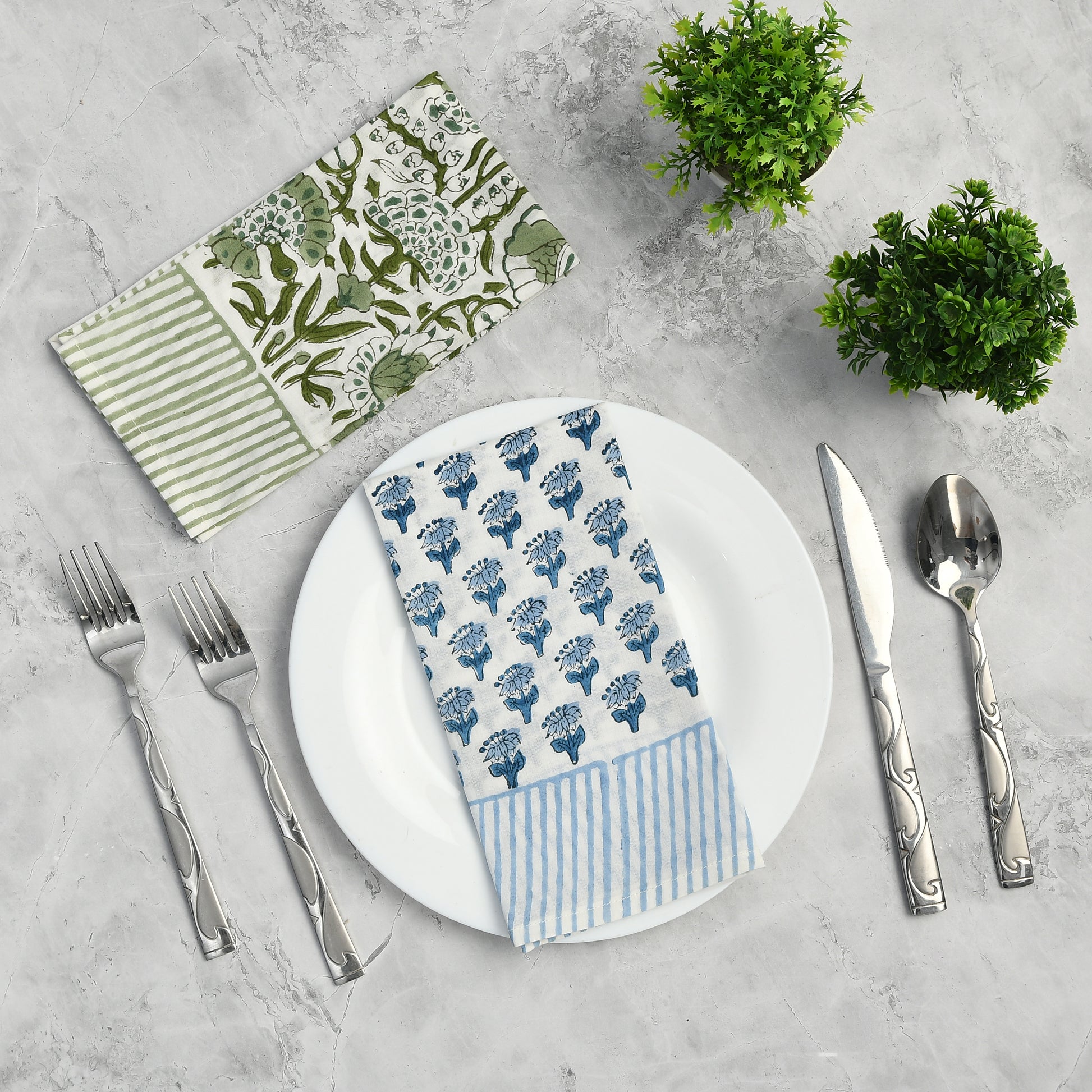 Single blue floral napkin folded under silverware on a white plate.