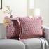 Two pink floral block print throw pillows with ruffled edges on a white sofa beside a modern lamp.