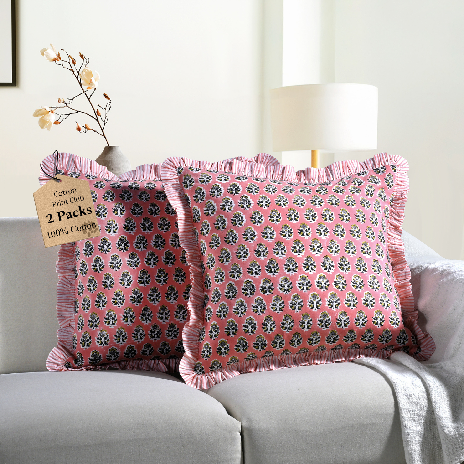 Two pink floral block print throw pillows with ruffled edges on a white sofa beside a modern lamp.