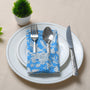 Single blue floral napkin folded under silverware on a white plate.

