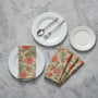 A set of folded cotton cloth napkins with a floral pattern, displayed on a table alongside a plate with cutlery.