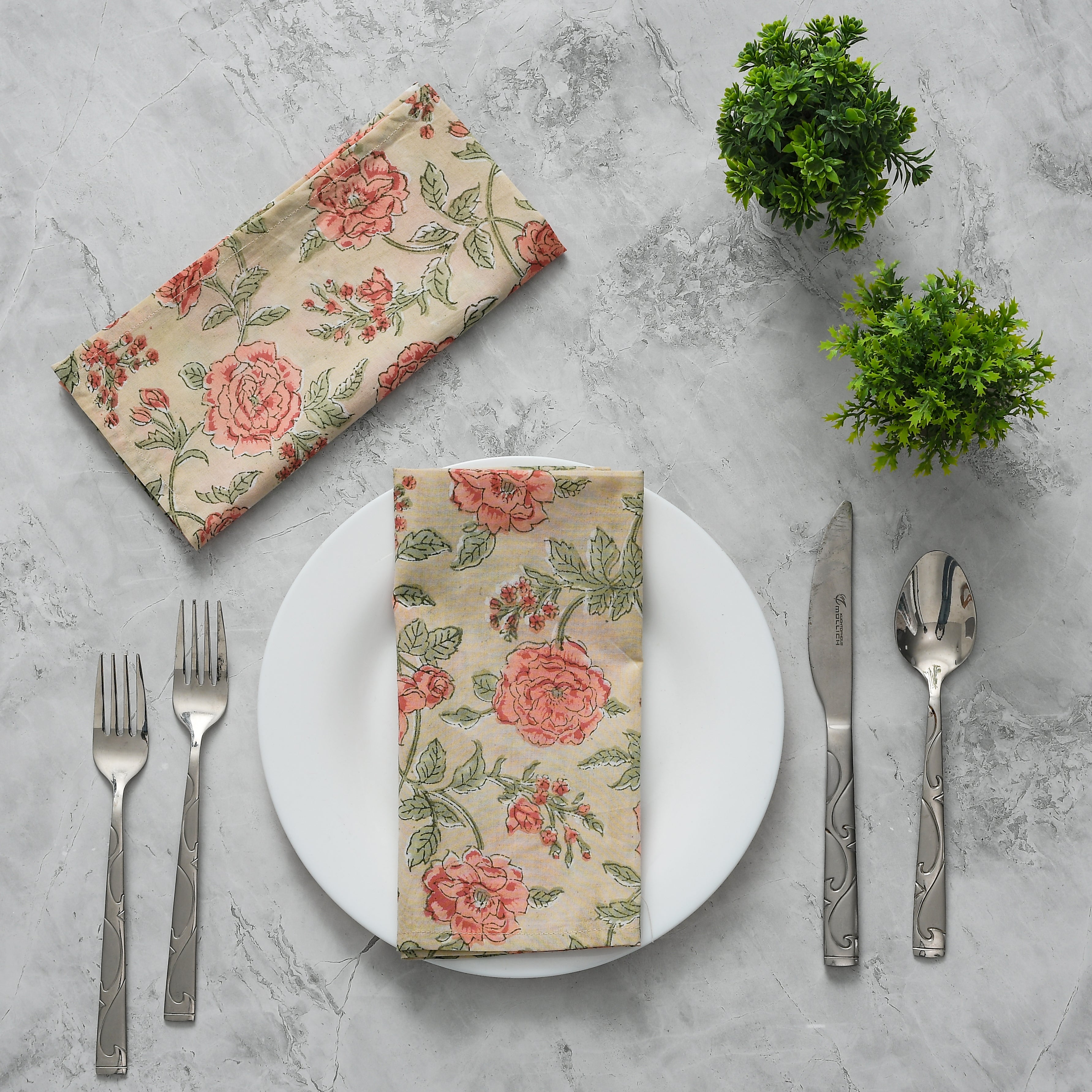 Elegant place setting with two pink and tan floral napkins and silverware arranged creatively.