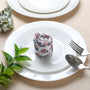 Rolled multicolor napkin on white plate with green foliage and fork.

