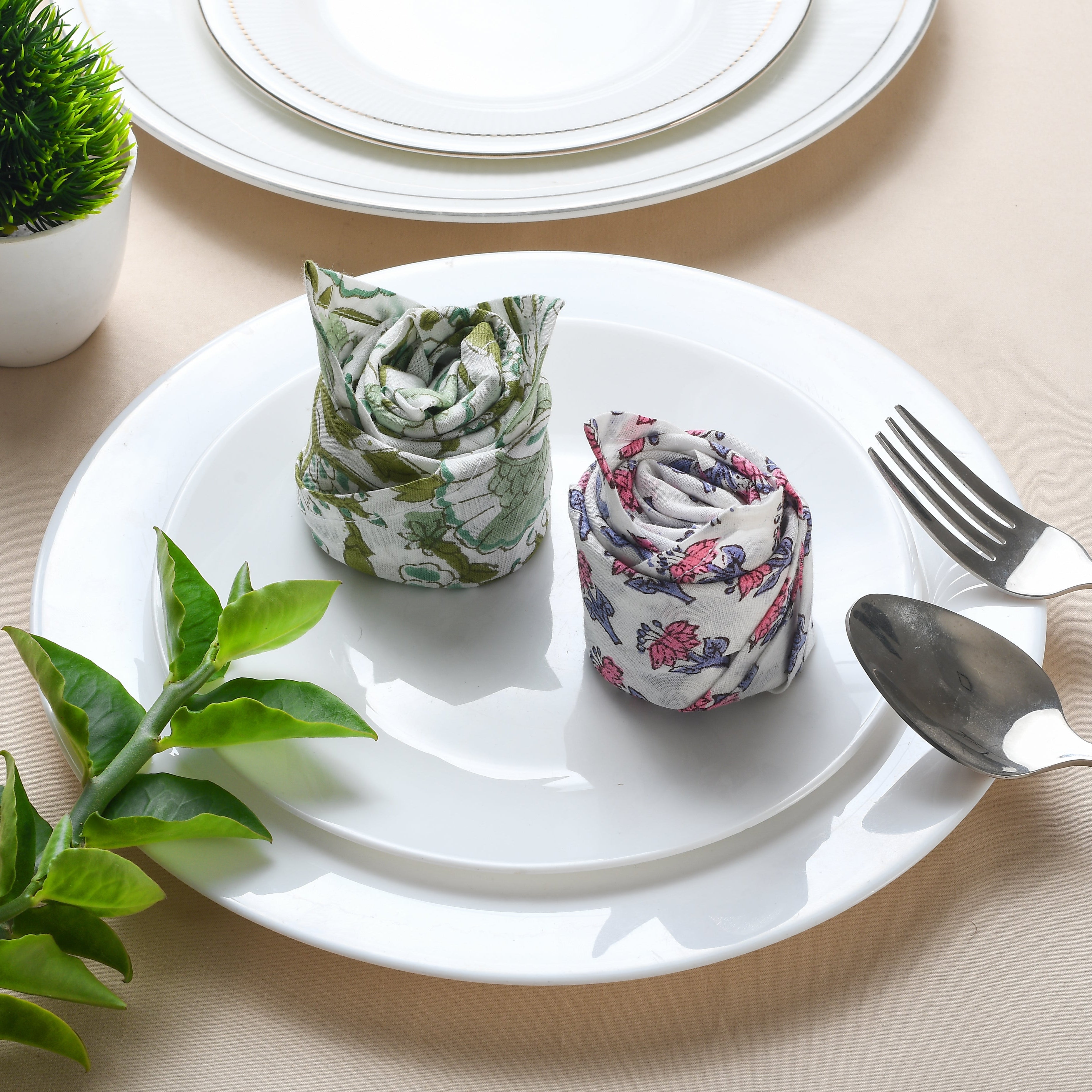 Rolled floral napkin placed on white plate with green leaf decoration.

