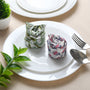 Rolled floral napkin placed on white plate with green leaf decoration.


