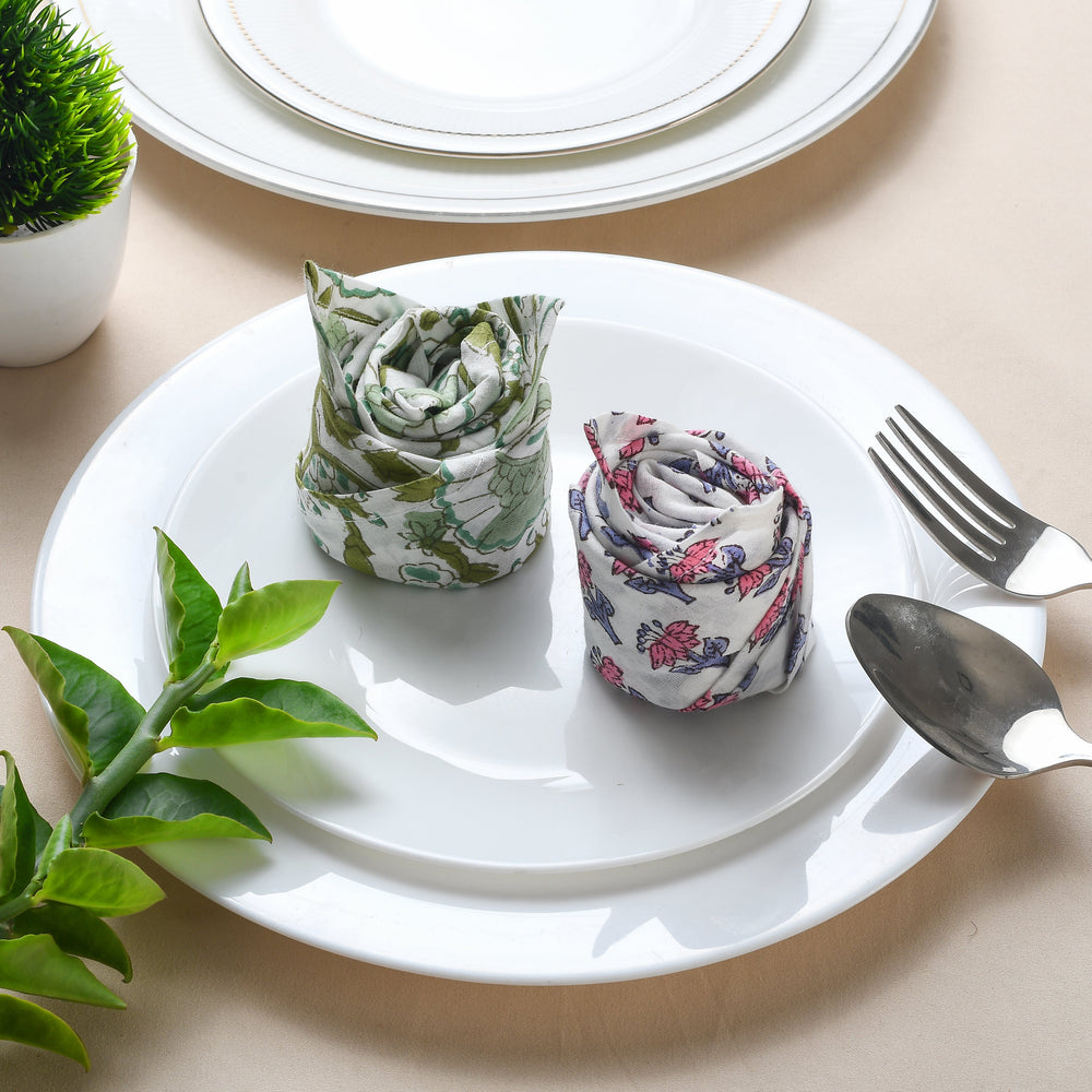 Rolled floral napkin placed on white plate with green leaf decoration.

