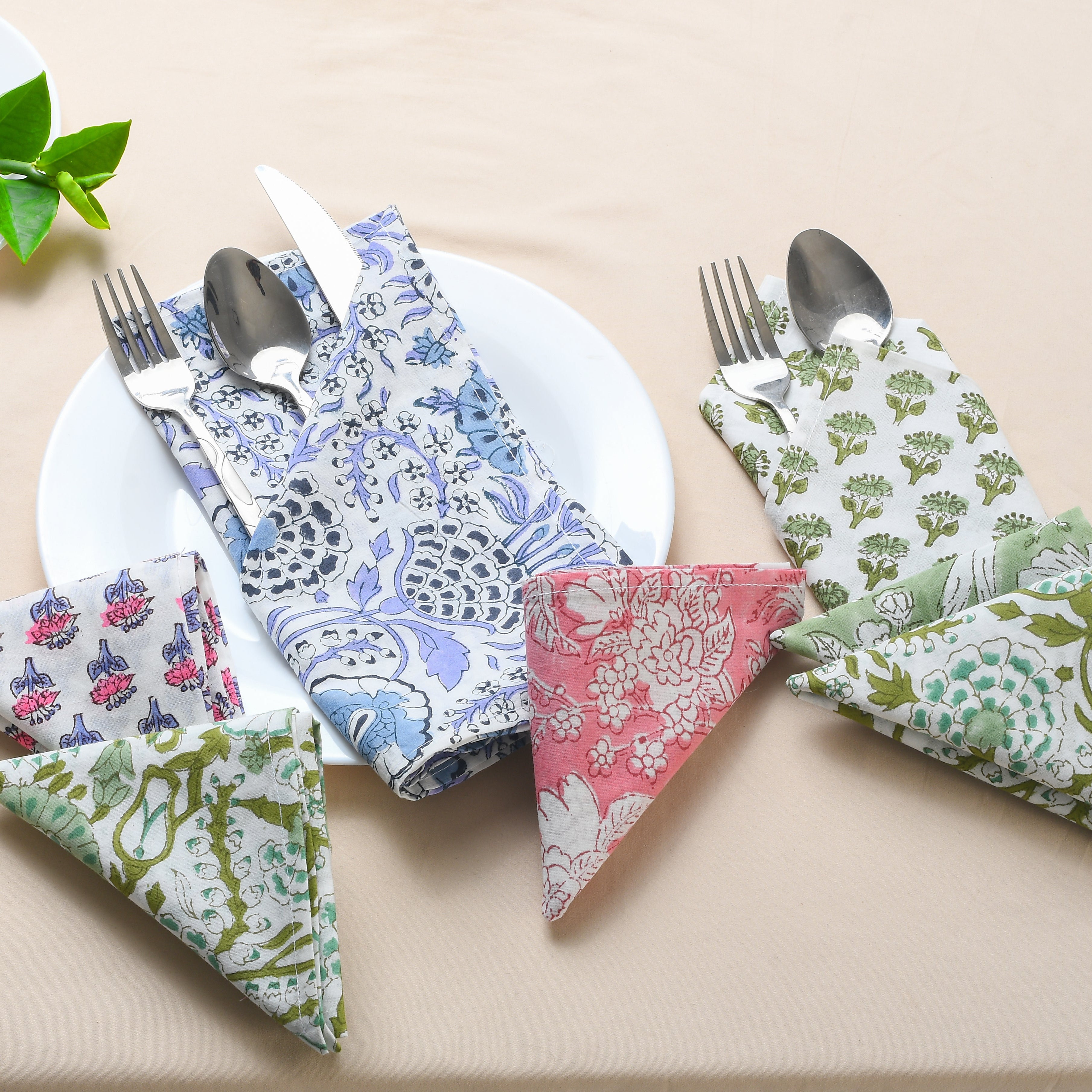 A set of cotton cloth napkins in various floral and geometric prints, displayed on a table with cutlery.