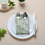 Single green floral napkin wrapped around silverware on a white plate.
