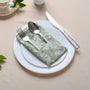Single green floral napkin wrapped around silverware on a white plate.