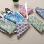 Four cotton napkins in assorted floral prints folded with silverware on a white plate.

