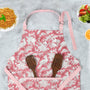 pink and white kitchen apron laying on the counter with wooden kitchen utensils in the front pocket