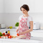 lady wearing a pink and white kitchen apron with wooden kitchen utensils in the front pocket while cutting vegetables on a cutting board