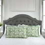 Gray upholstered headboard with green floral pillows on a bed in a bedroom setting.