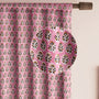 Semi-sheer cotton block print curtains in poppy pink with intricate patterns, hanging in a room with a light filtering through.