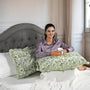 Woman sitting on a bed with green patterned pillows and a gray headboard.