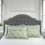 Green patterned pillows on a bed with a gray upholstered headboard.