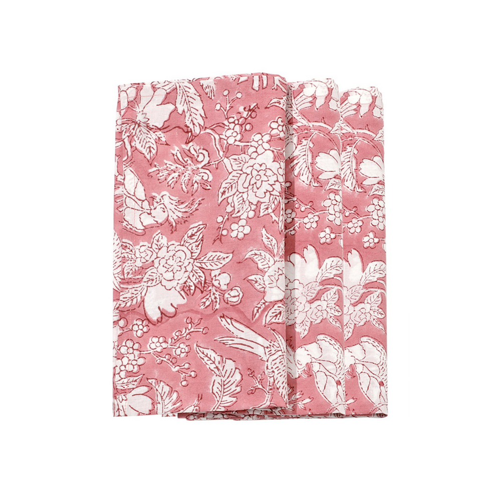 A folded coral pink cotton cloth napkin with white floral and geometric patterns.